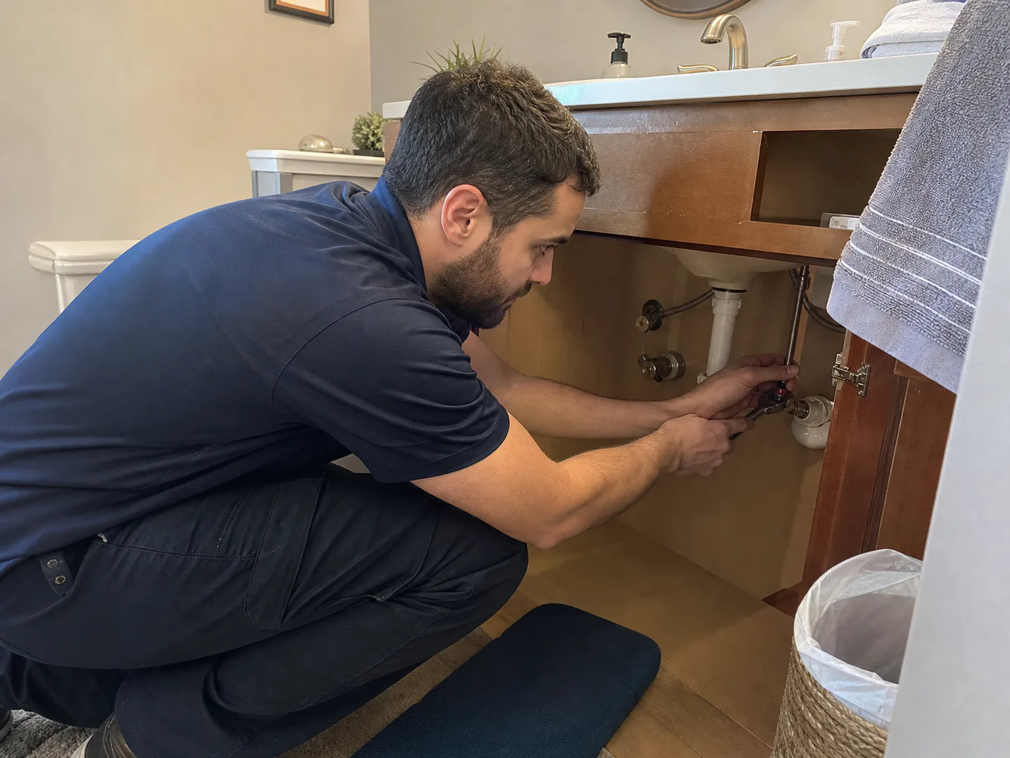 Plumber making a fixture supply connection inside a bathroom vanity