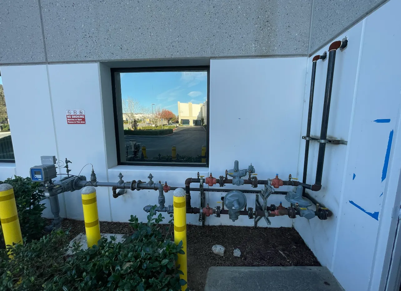 A plumber working on a residential gas line leak services job — mid-task, hands, tools and the work itself in sharp focus, the rest of the space softly out of focus