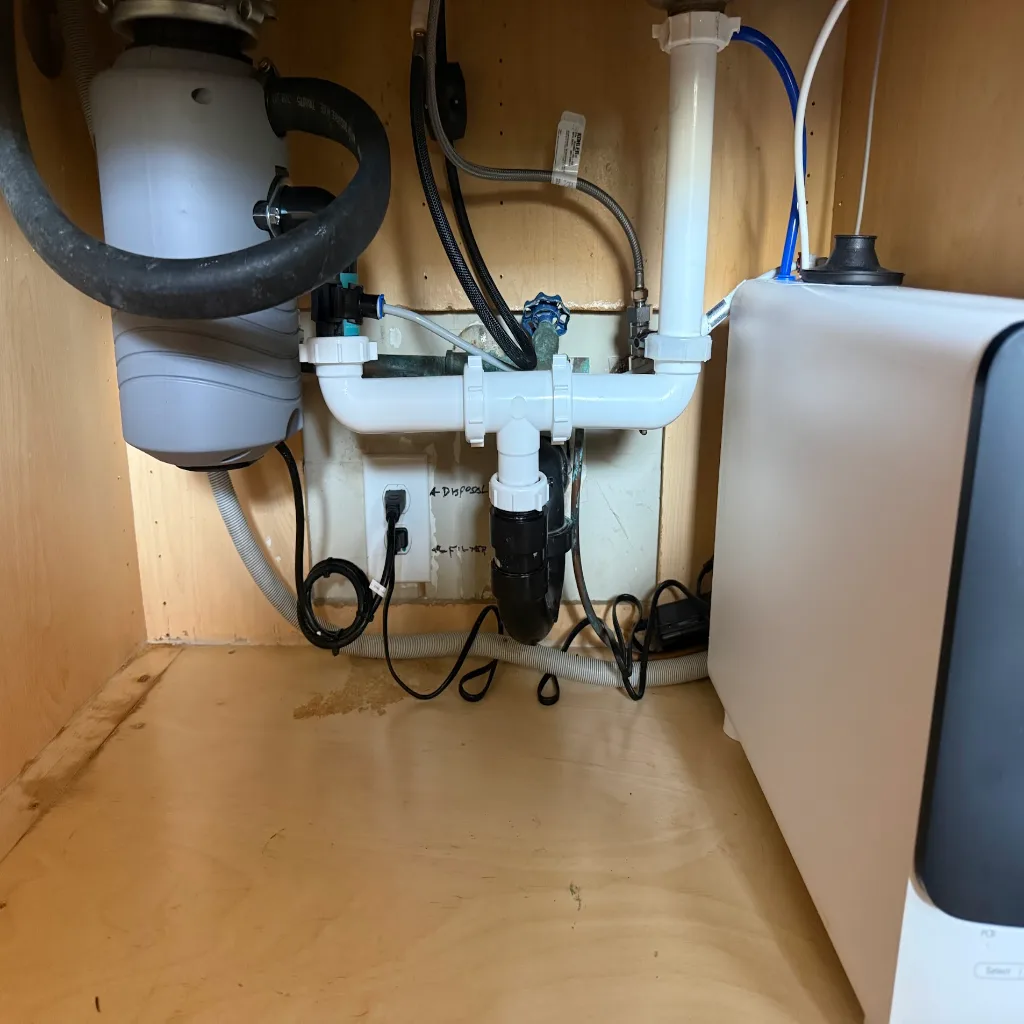 A set of tools — a drain machine and a pipe wrench — laid down on a clean surface beside the plumbing work they have just finished, everything tidy and put away