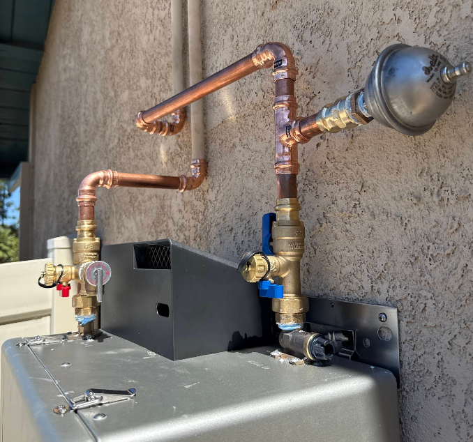 A plumber working on a residential water heater services job — mid-task, hands, tools and the work itself in sharp focus, the rest of the space softly out of focus